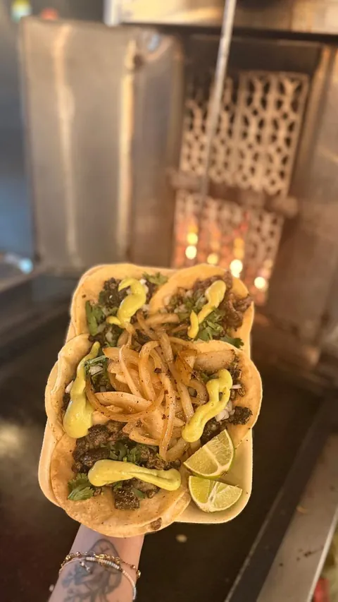 Orden de tacos de trompo negro con cebolla asada, guacamole y limón, frente al trompo encendido